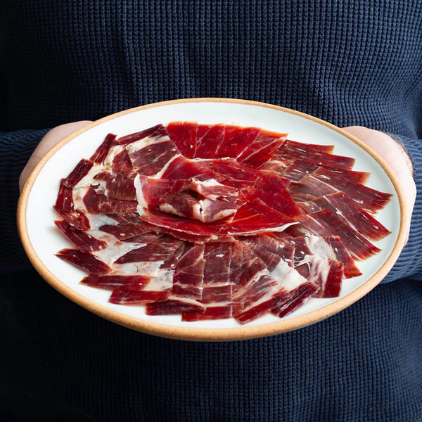 Tranches fines de jamón ibérico de bellota bien marbré sur une assiette, illustrant une coupe correcte pour une conservation optimale