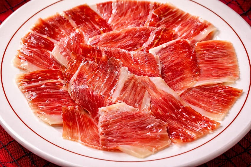Tranches de jambon ibérique de bellota avec brillance grasse sur assiette tempérée