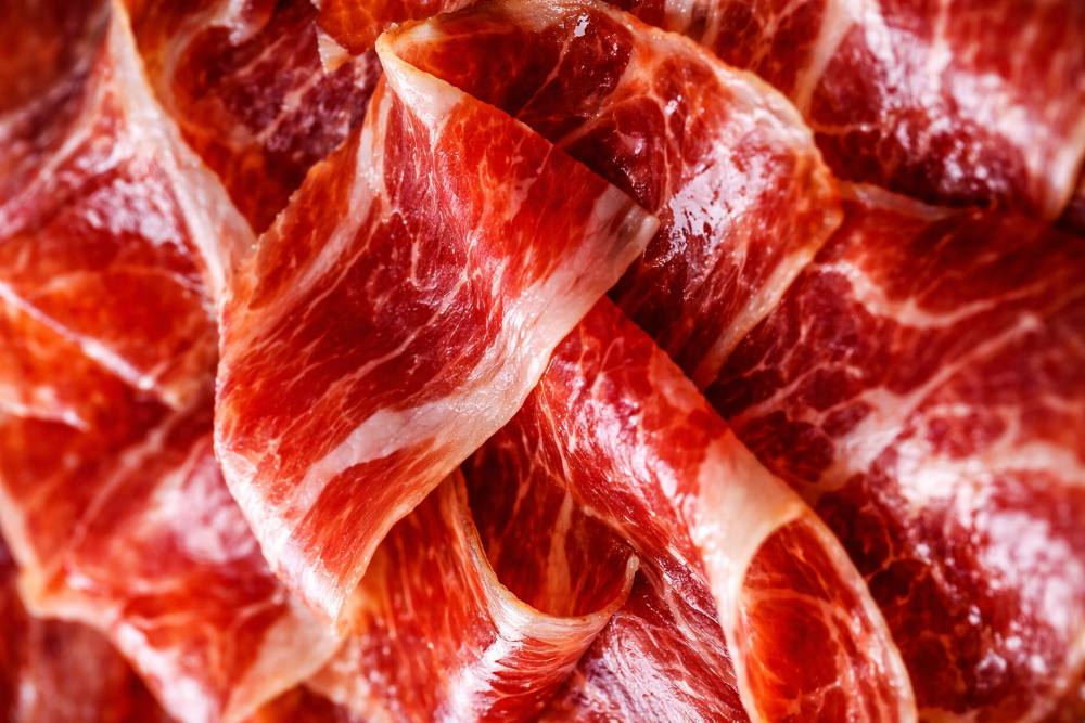 Tranches de jambon ibérique de bellota fraîchement coupées montrant le persillage de graisse intramusculaire