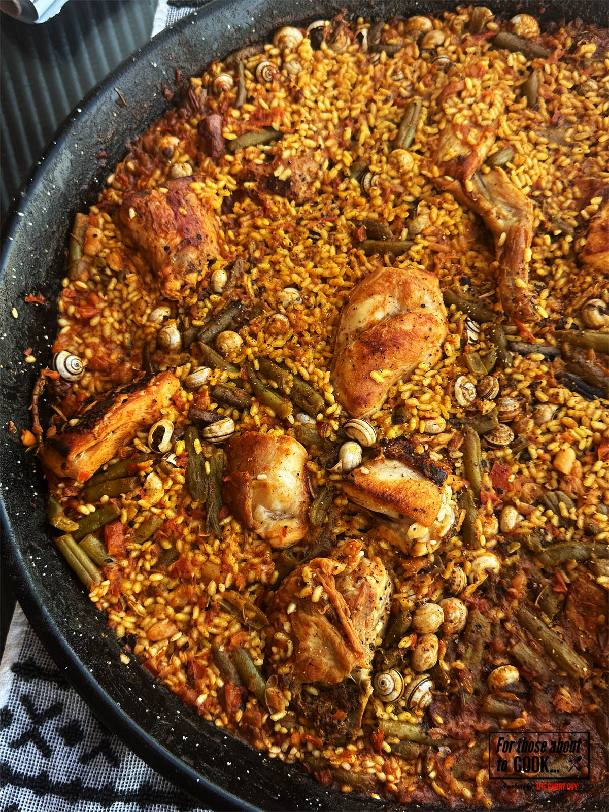 Paella valenciana tradicional cocinándose sobre fuego de leña con granos absorbiendo caldo