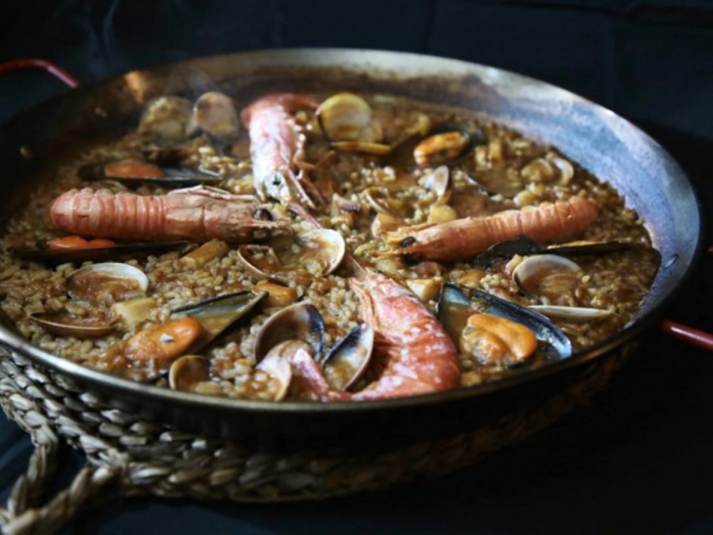Chef finalisant une paella gastronomique dans un restaurant contemporain