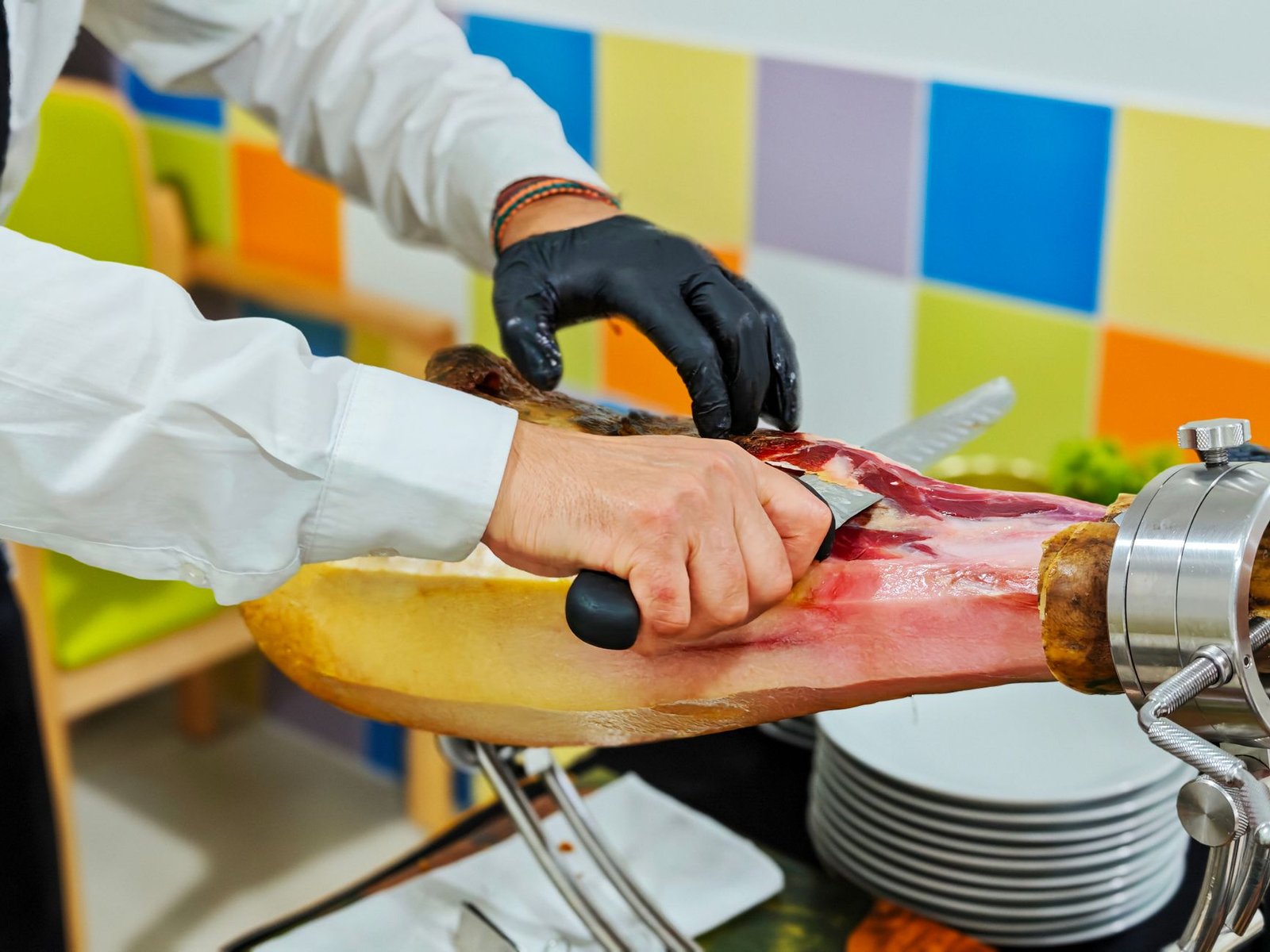 Mains de maître découpeur tranchant une patte ibérique avec un long couteau